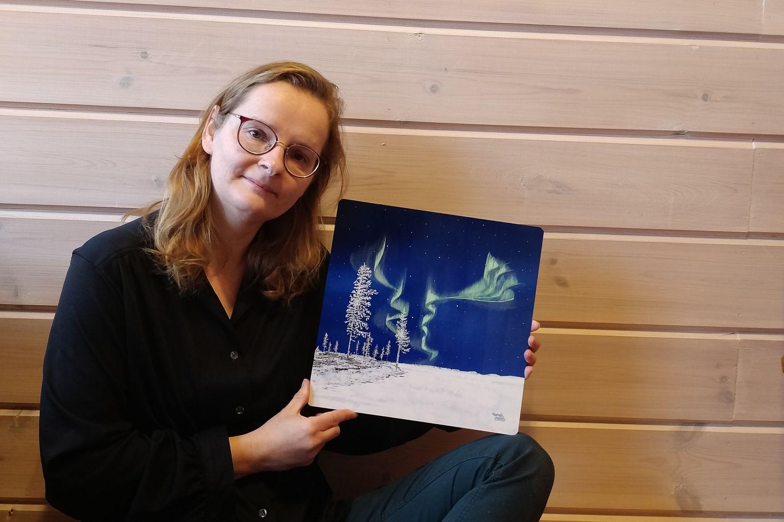 Els Bancken, illustrator behind Aurealis Creatief, holding a metal art print of Frozen Forest, the first season from the Lapland 8 Seasons collection.