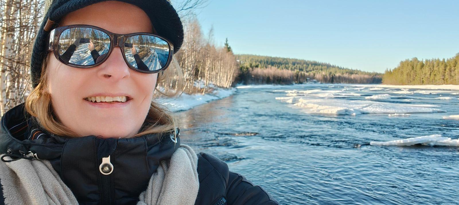 Els Bancken aan de rivier de Ounasjoki in Fins Lapland, eind april: vrij stromend water in het midden en drijvende ijsschotsen langs de oever onder een helderblauwe hemel.