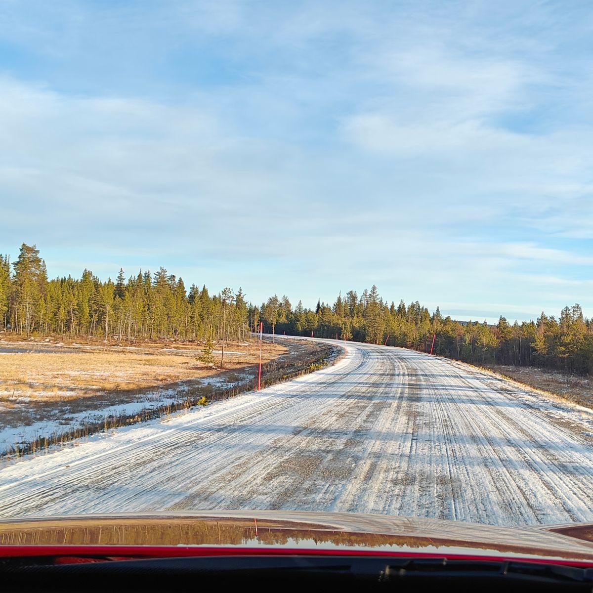 Uitzicht door de voorruit van een auto op een met sneeuw bestrooide weg in Fins Lapland eind oktober, de eerste sneeuw van het seizoen, met kaal gras langs de berm.