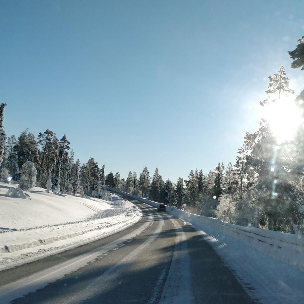 De laagstaande zon boven een met sneeuw bedekte weg en een bos in Lapland; het sneeuwoppervlak weerkaatst het licht in schitterende kristallen.