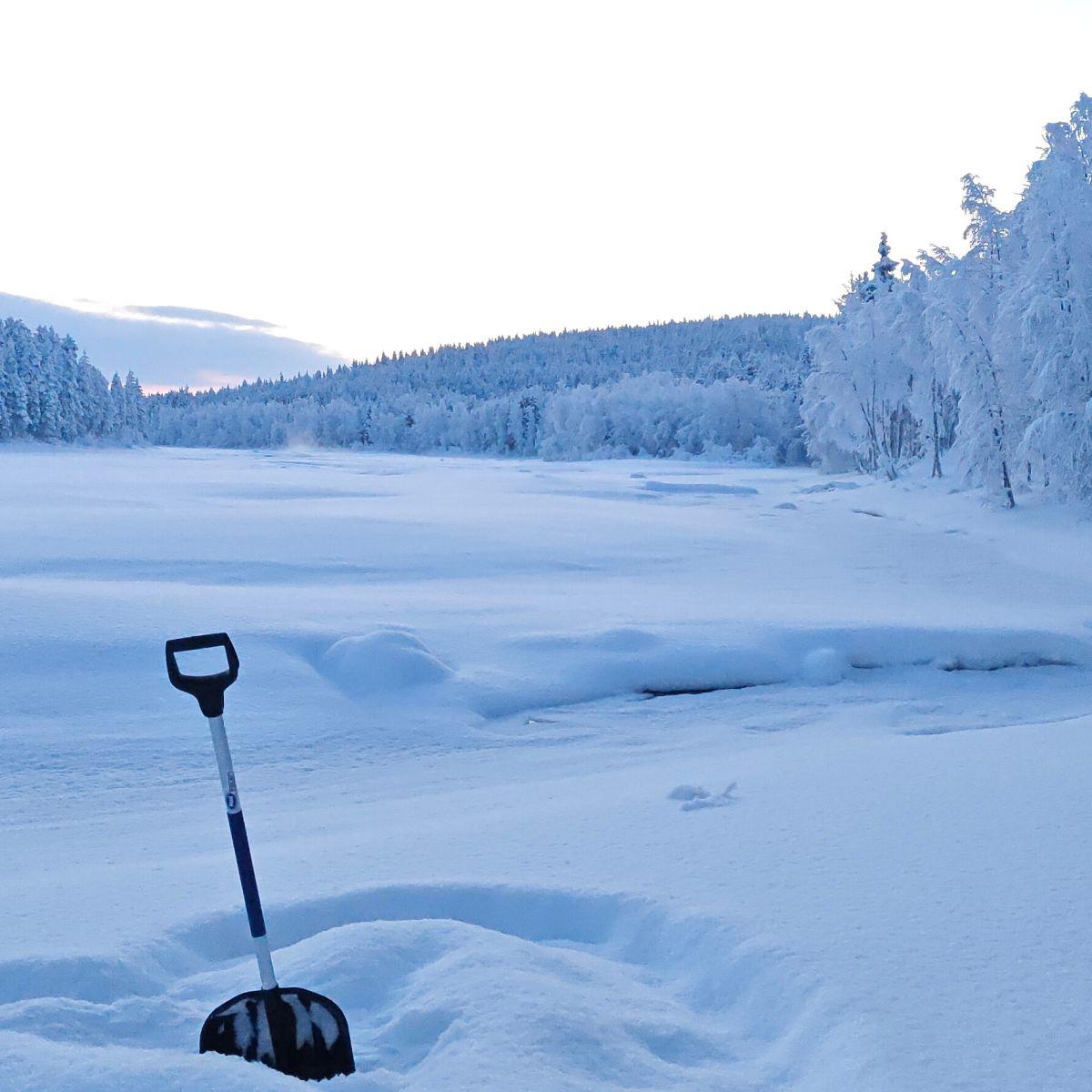 Een sneeuwschuiver die in de diepe sneeuw naast een bevroren rivier in Lapland staat, het bos bedekt met een dikke laag rijp onder een bleke winterhemel.