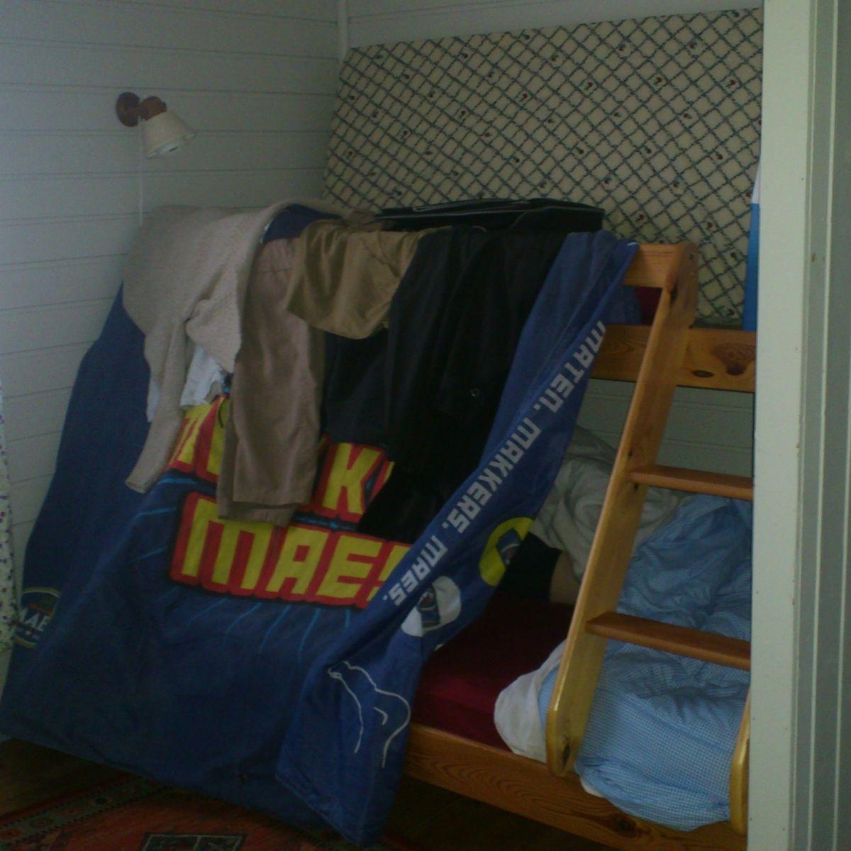Een geïmproviseerd verduisteringsdoek, gemaakt van een dekbed dat over de reling van een stapelbed in een Noorse rorbu-hut is gedrapeerd, om tijdens het slapen het licht van de middernachtzon buiten te houden.