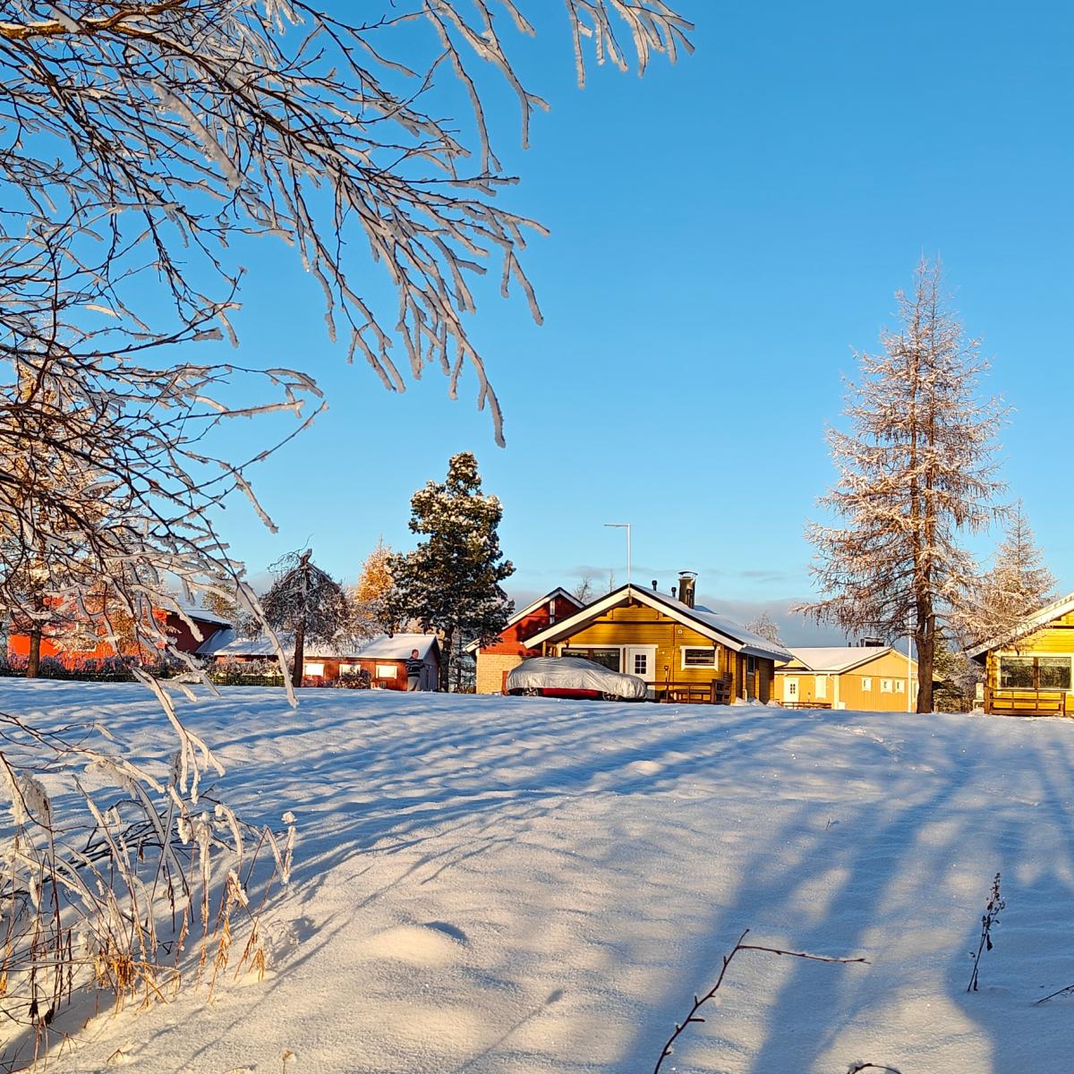 Een geel houten boerderijhuisje in een besneeuwd grasland naast de stroomversnellingen van de Ounasjoki, vlakbij Tepasto in Lapland.